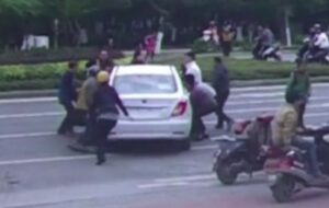 Passers-by lift car to free trapped cyclist CCTV still (YouTube).JPG