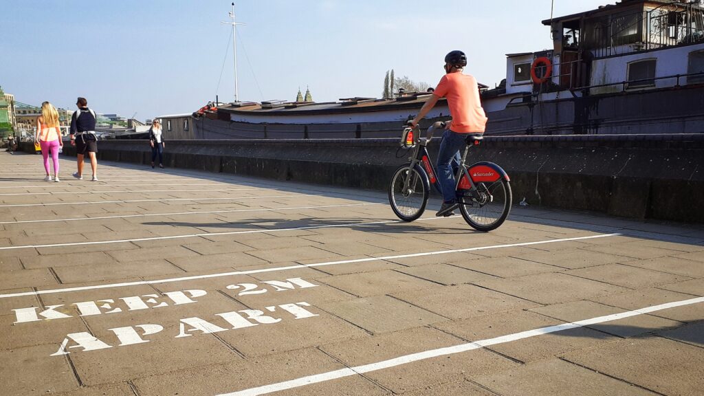 coronavirus – cyclists rides past social distance warning