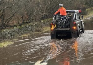 4×4 driver helps club cyclists across flooded section of road