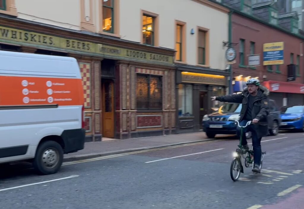 Cyclist riding past Belfast cycle lane blocked by parked cars for government cycle to work video (Department for Infrastructure) 2