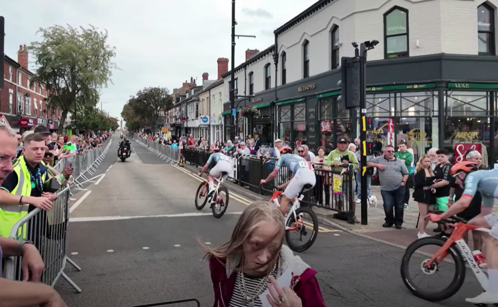 Woman crosses the road in front of peloton during 2026 Tour of Britain stage 2 2
