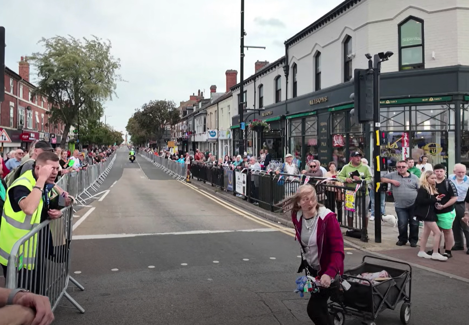 Woman crosses the road in front of peloton during 2026 Tour of Britain stage 2