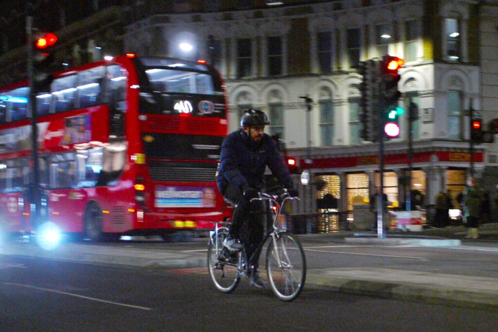 Cyclist in London at night with bus and red light in background