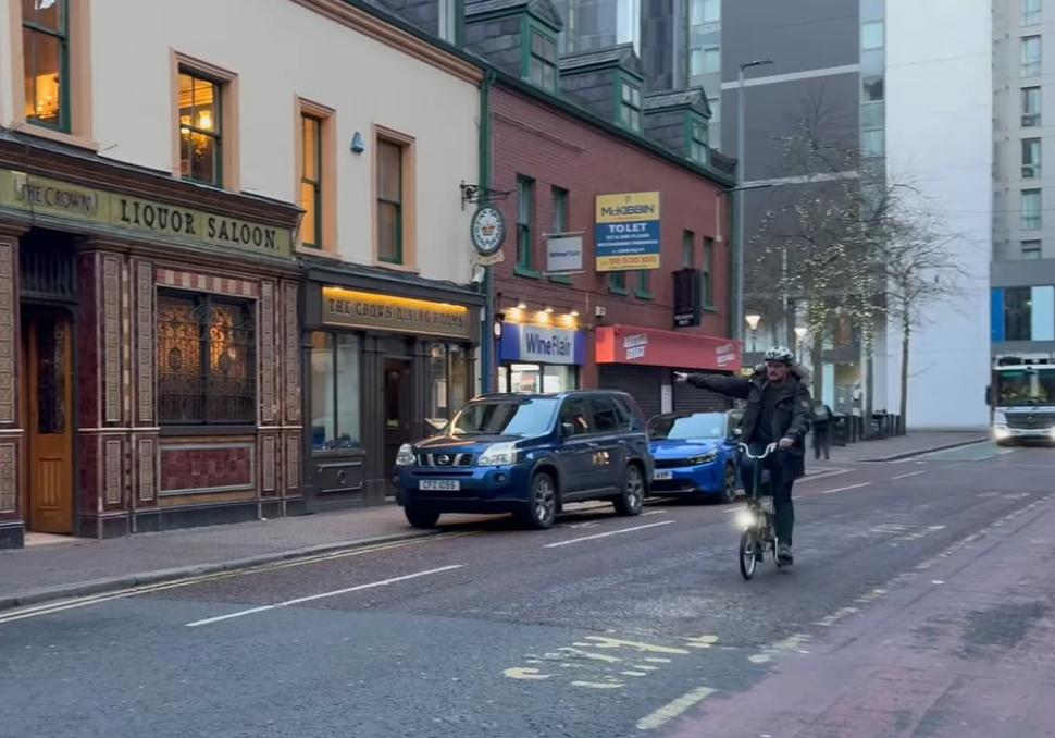 Cyclist riding past Belfast cycle lane blocked by parked cars for government cycle to work video (Department for Infrastructure)